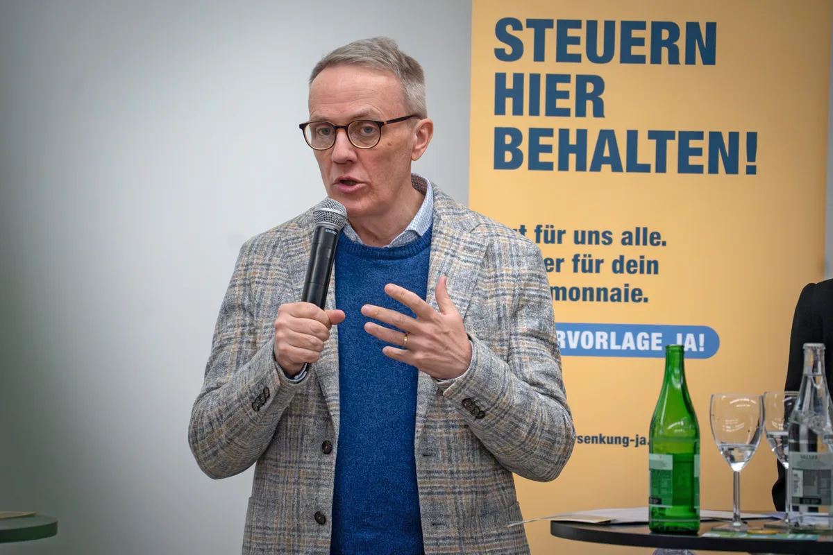 Ein Herr im Jackett und mit Brille am Mikrofon.